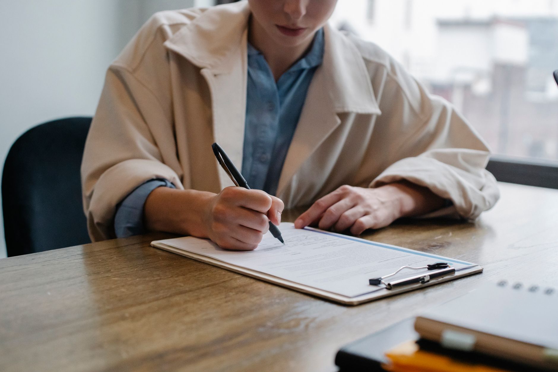 Personne remplissant un questionnaire de candidature sur un porte-documents, assise à une table
